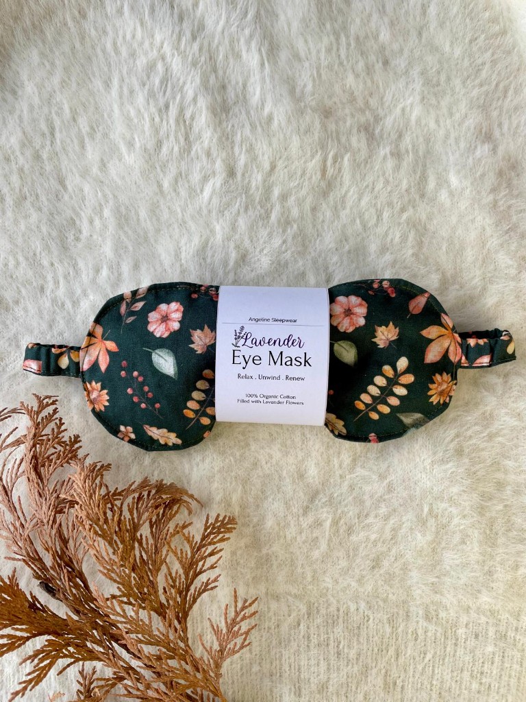A single eye mask in a dark green print of autumn leaves and berries.