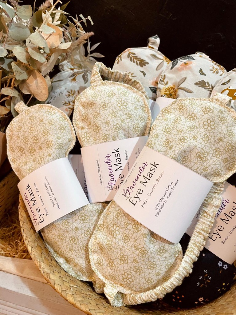 A basket of lavender eye masks in gold floral cotton, each banded in paper.