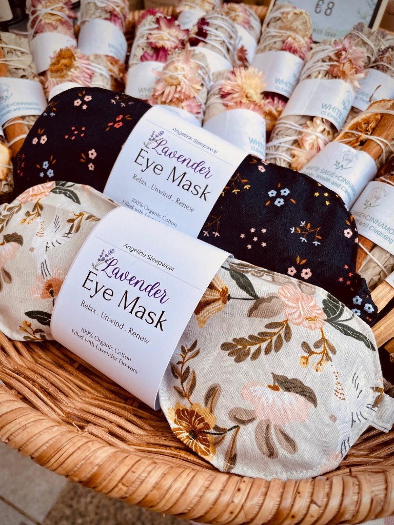 Two eye masks, one black with small flowers and one cream with large blooms, in a wicker basket.